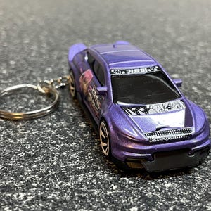 May include: Purple and white race car keychain with a cartoon character on the hood and the text "4th 키보드" on the roof.