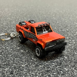 May include: Orange Hot Wheels toy truck with black wheels and a black roll cage. The truck has a black Hot Wheels logo on the side and a silver keychain attached.