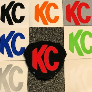 May include: A set of nine decals featuring the letters "KC" in various colors, including black, orange, red, blue, green, silver, and white. The decals are on a white background.