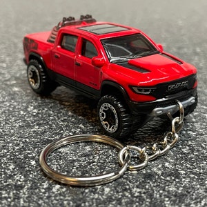May include: Red Ram 1500 TRX pickup truck keychain with a silver chain and a silver key ring. The truck has black accents and a black grill with the word "RAM" printed on it.
