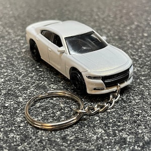 May include: White Dodge Charger keychain with a silver key ring and chain. The car is a miniature replica of a real car.