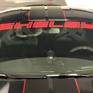 May include: A black car with red racing stripes and a red "SHELBY" windscreen banner.