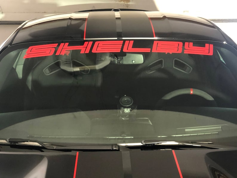 May include: A black car with red racing stripes and a red "SHELBY" windscreen banner.