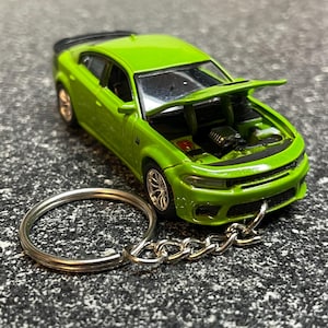 May include: A lime green toy car with the hood open, revealing the engine. The car is attached to a silver keychain. The car has black accents and silver rims. The keychain is made of a silver metal.