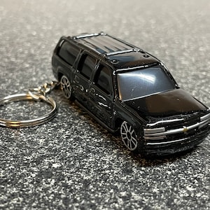 May include: Black Chevrolet Suburban keychain with a silver key ring. The keychain is a miniature replica of a full-size SUV.