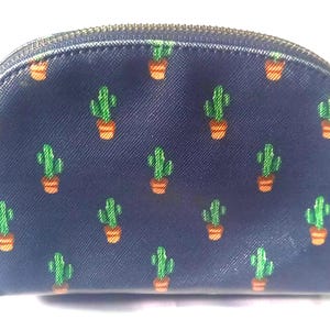 Puede incluir: Un neceser azul marino con un estampado repetido de cactus verdes en macetas naranjas. La bolsa tiene una cremallera dorada y una peque&ntilde;a leng&uuml;eta. La bolsa tiene forma redondeada.