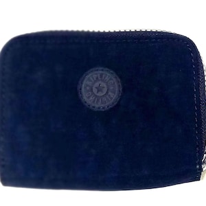 May include: A navy blue zippered wallet with a rounded shape. The wallet has a small, circular emblem on the front and a zipper pull. The material appears to be a soft, suede-like fabric.