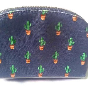 Puede incluir: Un neceser azul marino con un estampado repetido de cactus verdes en macetas naranjas. La bolsa tiene una parte superior curva, un cierre de cremallera y un peque&ntilde;o asa negra.