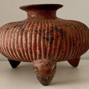 May include: A terracotta pot with three legs and a ribbed design. The pot is a reddish-brown colour with black streaks.