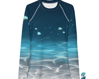 Puede incluir: Camiseta de protección solar de manga larga con un diseño oceánico azul y blanco. La camiseta presenta un patrón de peces y reflejos de agua. El logotipo de la marca "sardine42" es visible en la esquina inferior derecha. Cuello redondo blanco y costuras blancas.