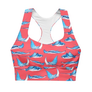 May include: Coral-colored sports bra featuring a repeating pattern of blue stingrays with white spots. The bra has a racerback design and is made of a smooth, likely athletic fabric. The overall theme is aquatic and marine life.