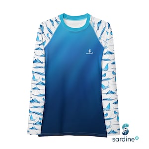 May include: A long-sleeved rash guard shirt with a blue gradient design. The sleeves feature a pattern of blue manta rays on a white background. The shirt has the brand name "sardine" printed on the front.