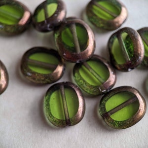 May include: Close-up of several oval-shaped beads. Each bead features a bright green center and a bronze-colored, oval frame. A dark line bisects the green center. These beads are ideal for jewelry making.