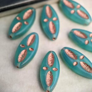 May include: Teal blue oval-shaped glass beads with a copper-colored design. The beads have a glossy finish and are perfect for jewelry making.