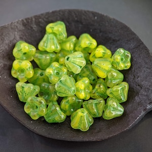 May include: A collection of green and yellow glass beads in the shape of a flower. The beads are arranged in a bowl.
