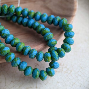 May include: A strand of blue and green glass beads with a speckled pattern. The beads are round and have a slightly irregular shape.