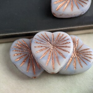 May include: Three white heart-shaped glass beads with a copper-colored starburst design.