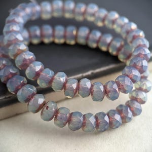 May include: Strands of faceted beads in shades of pale blue and mauve. The beads are strung together, forming a circular shape. The beads have a multifaceted design, reflecting light and creating a shimmering effect. The beads are likely used for jewelry making.