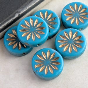 May include: Six round, turquoise glass beads with a gold floral design. The beads are arranged in a cluster, showcasing their glossy finish and intricate detailing. These beads are ideal for jewelry making.