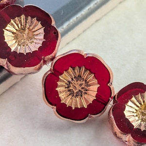 May include: Close-up of several red flower-shaped beads with a gold-colored center. The beads have a metallic finish and are arranged in a row. The petals are a deep red color.