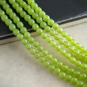 May include: A strand of round, green glass beads with a glossy finish. The beads are strung on a clear thread and are arranged in rows.