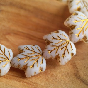 May include: A strand of white glass beads with gold leaf accents in the shape of maple leaves.