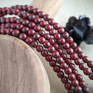 May include: A strand of red and black speckled round beads. The beads are strung on a cord and are arranged in a pile.