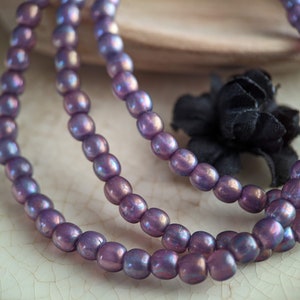May include: A strand of iridescent purple glass beads. The beads are round and have a smooth, polished finish. The beads are strung on a clear thread.