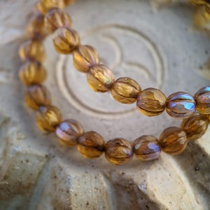 May include: Two strands of brown glass beads with a faceted, pumpkin-shaped design. The beads have a subtle iridescent sheen.