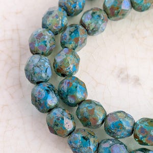 May include: Strands of faceted beads in shades of blue, green, and brown. The beads have a mottled, textured appearance with a metallic sheen. The beads are strung together, suggesting they are for jewelry making.