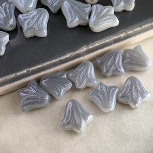 May include: A collection of gray glass flower-shaped beads with a pearlescent finish. The beads have a delicate, intricate design.