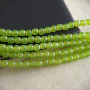 May include: A strand of lime green glass beads. The beads are round and have a slightly iridescent finish.
