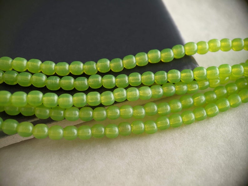May include: A strand of lime green glass beads. The beads are round and have a slightly iridescent finish.