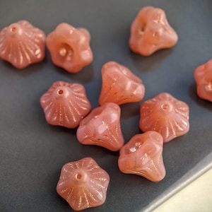 May include: A group of ten pink glass beads with a starburst design. The beads are arranged in a cluster on a gray surface.