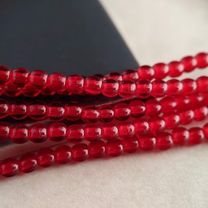 May include: A close-up of a strand of red glass beads. The beads are round and have a slight shine to them.