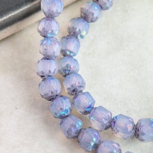 May include: Close-up of two strands of iridescent, faceted beads. The beads are a pale lavender color with a shimmering, multi-colored finish. The beads are strung together, creating a delicate and elegant appearance. Ideal for jewelry making.