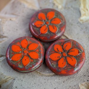 May include: Three round orange glass buttons with a floral design. The buttons have a mottled brown and green background.