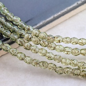 May include: Strands of olive green glass beads with a swirled pattern. The beads are oval-shaped and have a translucent quality, with a mix of light and dark green hues. These beads are suitable for jewelry making.