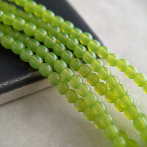 May include: A strand of light green glass beads. The beads are round and have a smooth, polished finish.
