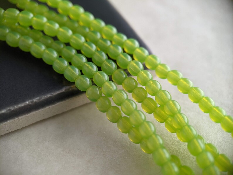 May include: A strand of light green glass beads. The beads are round and have a smooth, polished finish.