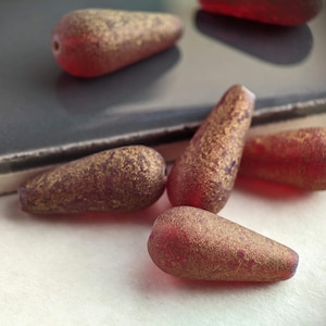 May include: Five red glass beads with gold flecks. The beads are teardrop shaped and have a glossy finish.