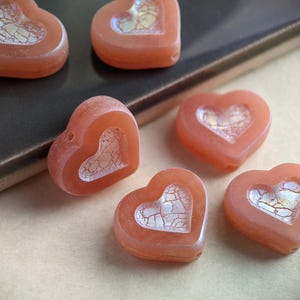 May include: Six heart-shaped glass beads with a white crackle design inside. The beads are a light orange color.