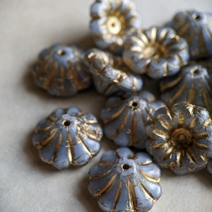 May include: A group of blue glass beads with gold accents. The beads are shaped like flowers with a raised center and multiple petals. The beads are arranged in a pile on a white surface.