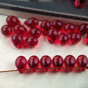 May include: A collection of red glass beads in the shape of teardrops. The beads are strung on a gold wire.