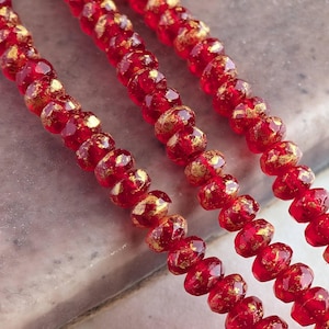 May include: Strands of faceted red beads with gold flecks. The beads are strung together, creating a textured and eye-catching design. The beads are a deep red color, with a glossy finish. The gold flecks add a touch of sparkle and elegance to the beads.
