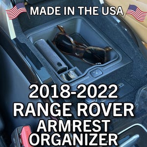 May include: Black Range Rover armrest organizer for 2018-2022 models. The organizer includes compartments for sunglasses, coins, and other small items. The text "MADE IN THE USA" is displayed.