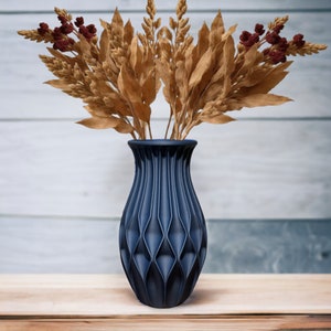 May include: A dark blue ceramic vase with a geometric pattern, holding dried brown wheat stalks with red berries.