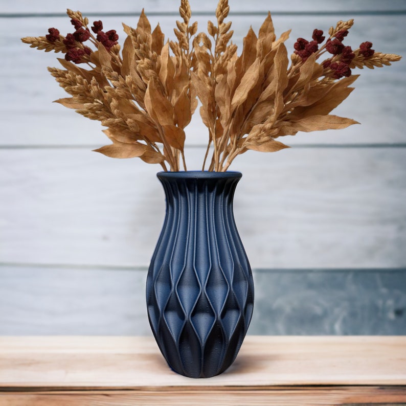 May include: A dark blue ceramic vase with a geometric pattern, holding dried brown wheat stalks with red berries.