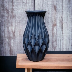 May include: A dark blue ceramic vase with a geometric, diamond-shaped pattern. The vase has a wide base and a narrow neck.