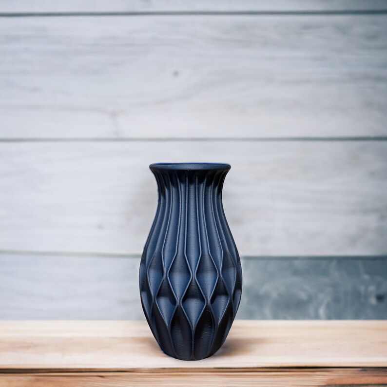 May include: A dark blue ceramic vase with a geometric, diamond-shaped pattern. The vase has a wide base and a narrow neck.